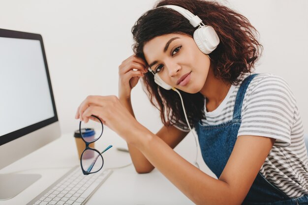 Mujer joven en camisa de rayas con piel de color marrón claro y grandes ojos oscuros posando mientras trabaja con la computadora