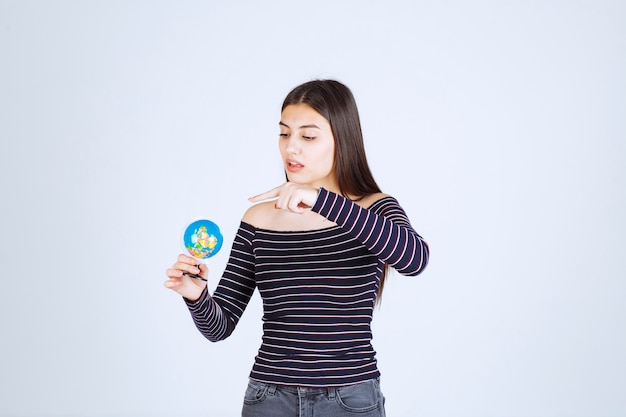 Mujer joven en camisa a rayas sosteniendo un mini globo y adivinando un lugar sobre él