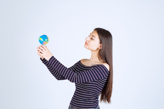 Mujer joven en camisa a rayas sosteniendo un mini globo y parece emocionado