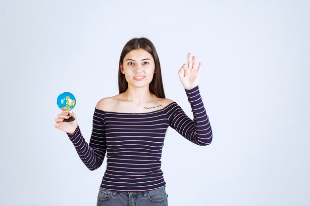 Mujer joven en camisa a rayas sosteniendo un mini globo y parece emocionado