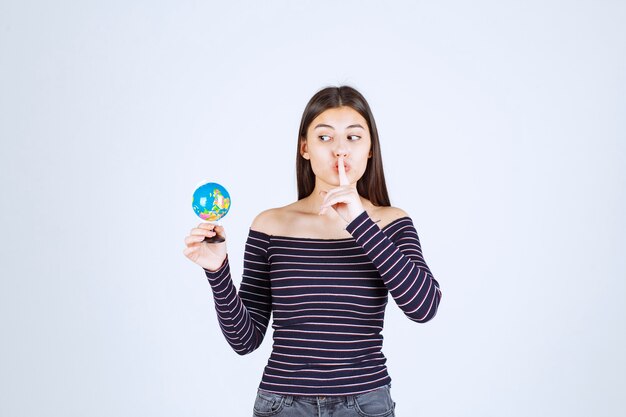 Mujer joven en camisa a rayas sosteniendo un mini globo y pidiendo silencio