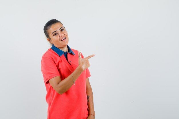 Mujer joven con camisa roja apuntando a la derecha con el dedo índice y mirando bonita vista frontal.