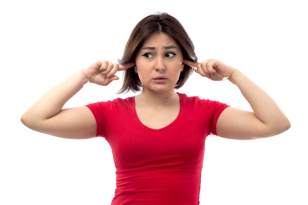 Mujer joven en camisa roja con expresión preocupada cubriendo sus oídos