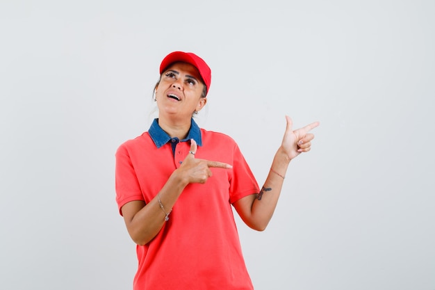 Mujer joven con camisa roja y gorra apuntando a la derecha con los dedos índices y mirando pensativo, vista frontal.