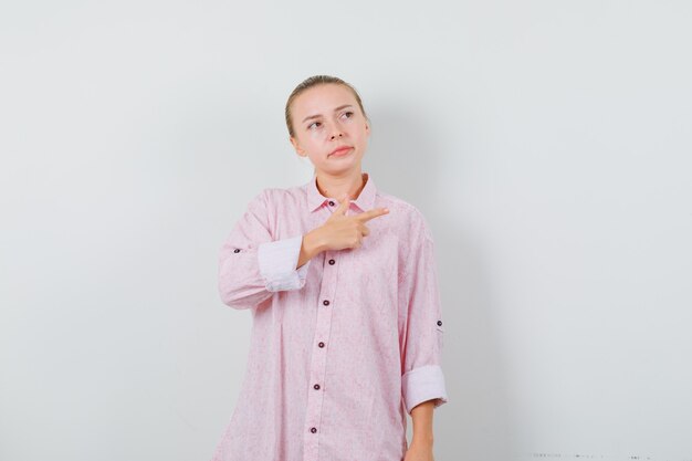 Mujer joven en camisa rosa apuntando hacia un lado y mirando insatisfecho