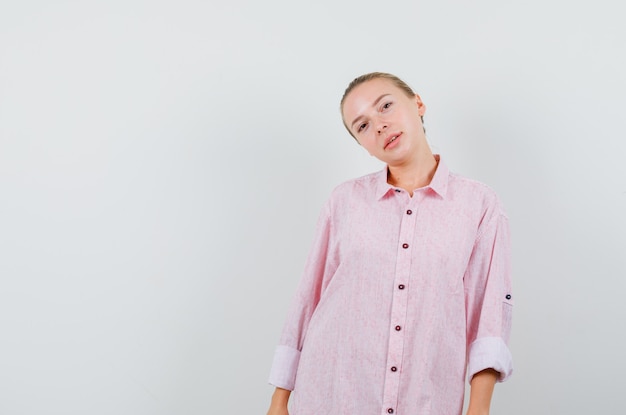 Mujer joven en camisa rosa inclinando la cabeza sobre el hombro