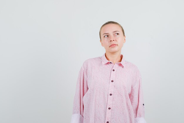 Mujer joven en camisa rosa mirando hacia arriba y mirando pensativo