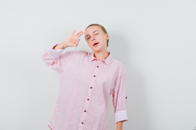 Mujer joven en camisa rosa mostrando signo ok y guiño de ojo