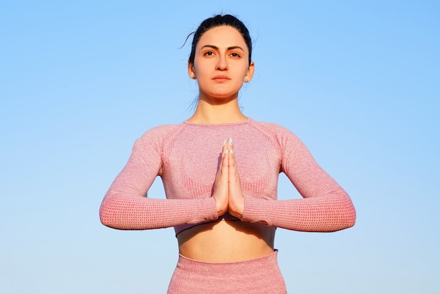 Mujer joven en camisa rosa y pantalones en la hierba durante el día dentro del parque verde meditando y haciendo yoga en diferentes poses