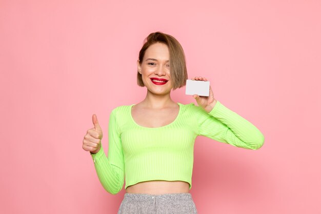 Mujer joven en camisa verde y falda gris sonriendo y sosteniendo una tarjeta gris