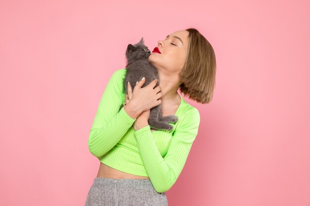 Mujer joven en camisa verde y pantalón gris con lindo gatito gris