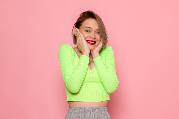 Mujer joven con camisa verde y pantalón gris posando con deleite y sonrisa en su rostro