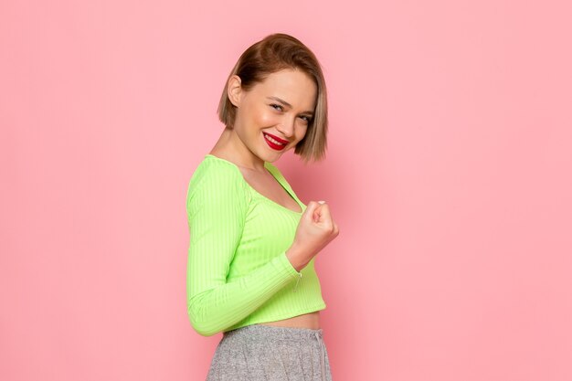 Mujer joven con camisa verde y pantalón gris posando con una sonrisa en su rostro