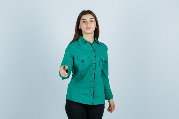 Mujer joven en camisa verde posando mientras estira la mano y mira desconcertado, vista frontal.