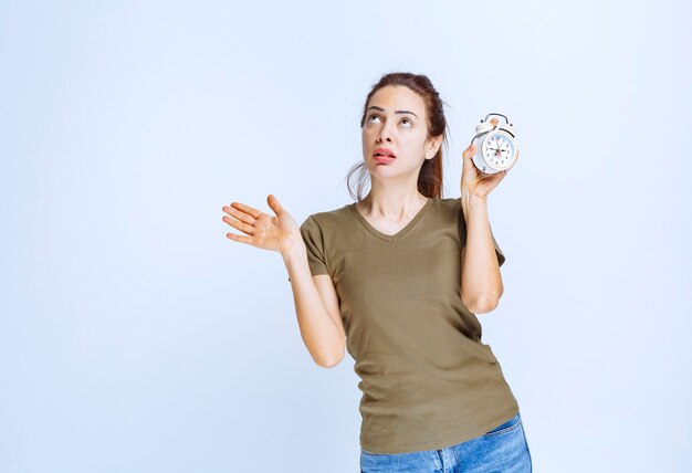 Mujer joven en camisa verde sosteniendo un reloj despertador y parece confundido