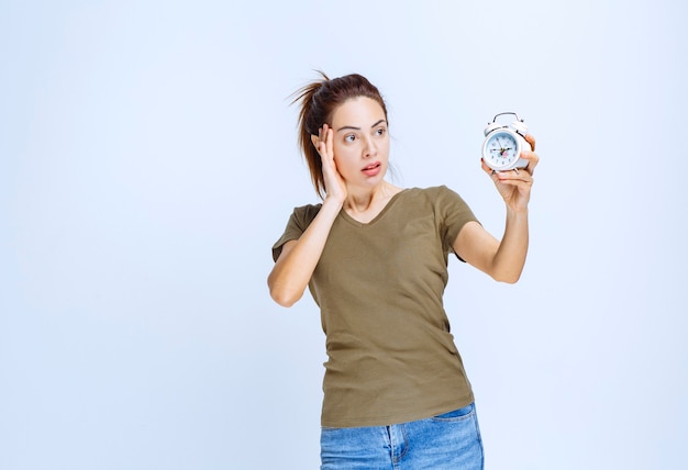 Mujer joven en camisa verde sosteniendo un reloj despertador y parece confundido