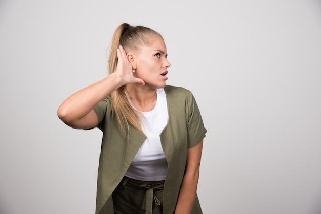 Mujer joven con camisa verde tratando de escuchar.