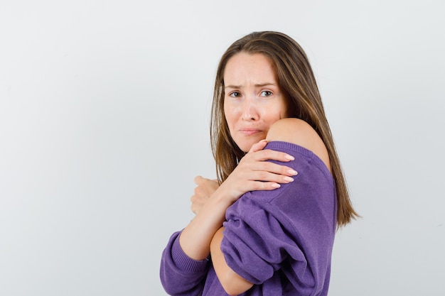 Mujer joven en camisa violeta abrazándose a sí misma y mirando ofendida.