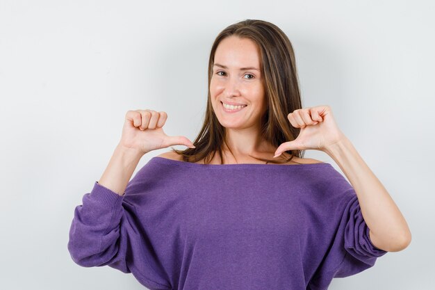 Foto gratuita mujer joven en camisa violeta apuntando a sí misma y mirando orgullosa, vista frontal.