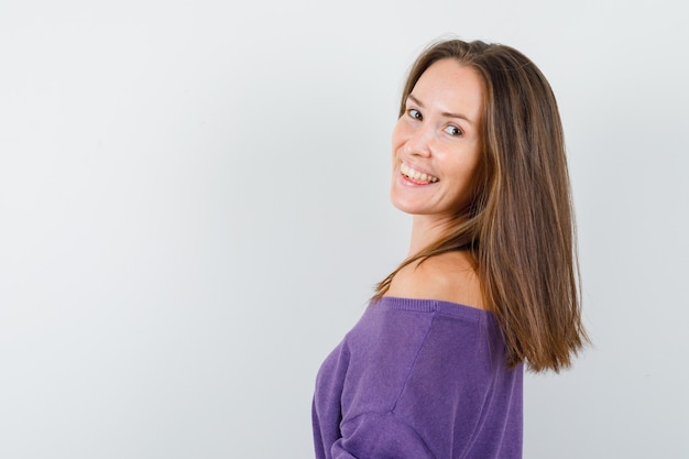 Foto gratuita mujer joven en camisa violeta mirando a cámara y mirando alegre.