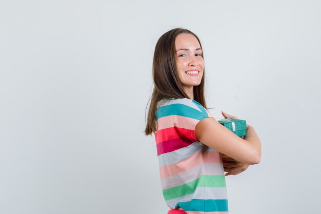 Mujer joven en camiseta abrazando cajas presentes y mirando alegre.