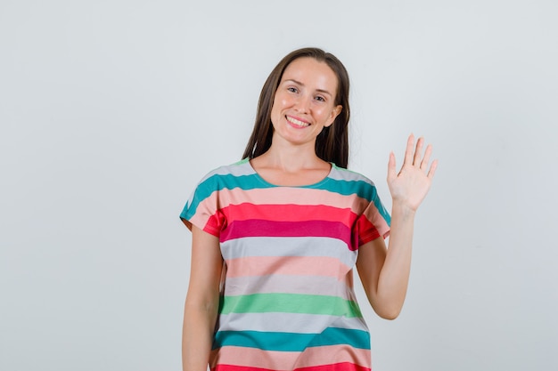 Foto gratuita mujer joven en camiseta agitando la mano para saludar y mirando alegre, vista frontal.