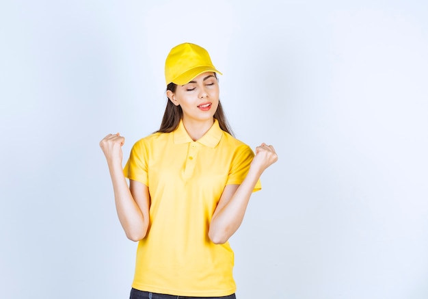 Mujer joven en camiseta amarilla y gorra de pie sobre fondo blanco.