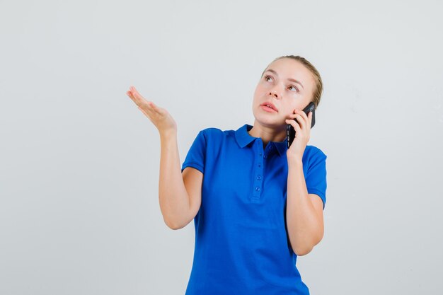 Mujer joven en camiseta azul hablando por teléfono móvil y mirando pensativo