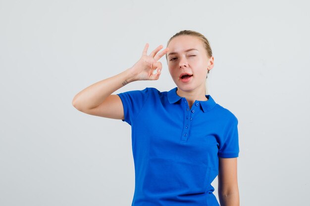 Mujer joven en camiseta azul mostrando gesto ok y guiño de ojo