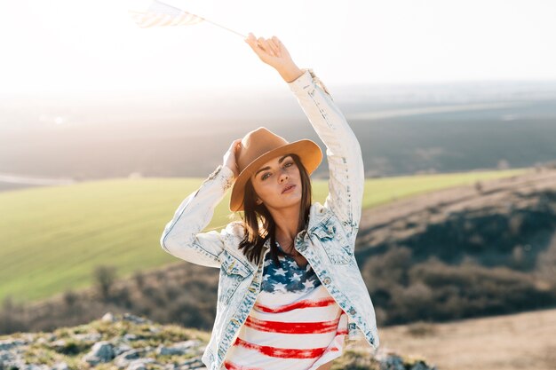 Mujer joven en camiseta de la bandera americana en la cima de la montaña