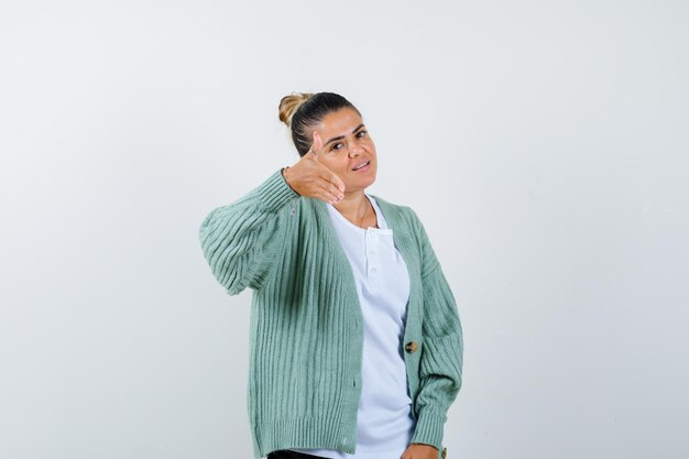 Mujer joven en camiseta blanca y chaqueta de punto verde menta que invita a venir y que parece feliz