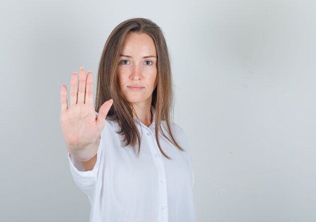 Mujer joven en camiseta blanca mostrando la palma a la cámara y mirando confiada