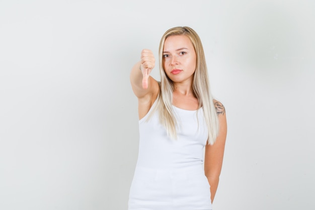 Mujer joven en camiseta blanca mostrando el pulgar hacia abajo y mirando disgustado