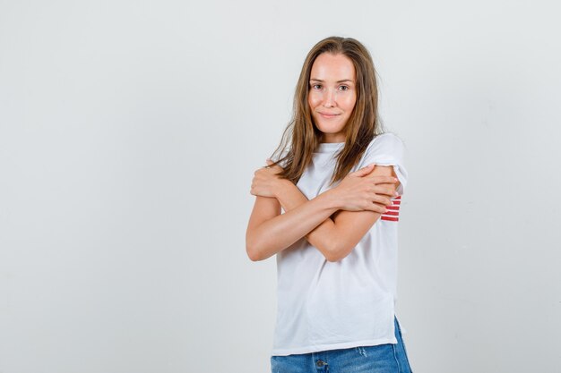 Mujer joven en camiseta blanca, pantalones cortos abrazándose y sintiendo frío