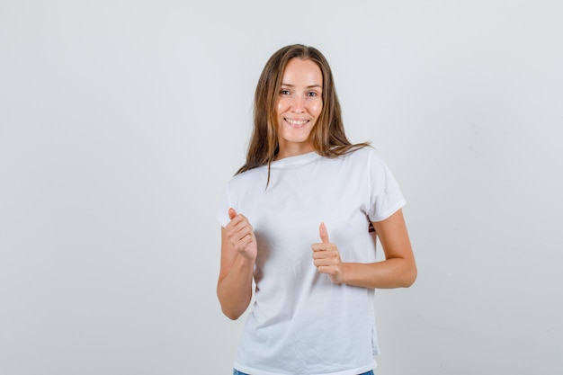 Mujer joven en camiseta blanca, pantalones cortos mostrando los pulgares hacia arriba y mirando feliz