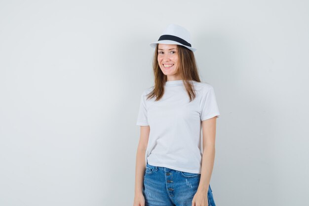 Mujer joven con camiseta blanca, pantalones cortos, sombrero y aspecto encantador.