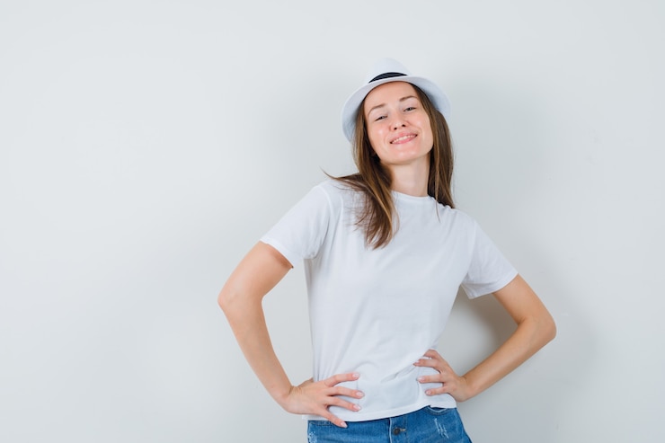 Foto gratuito mujer joven en camiseta blanca, pantalones cortos, sombrero posando mientras está de pie y parece seguro.