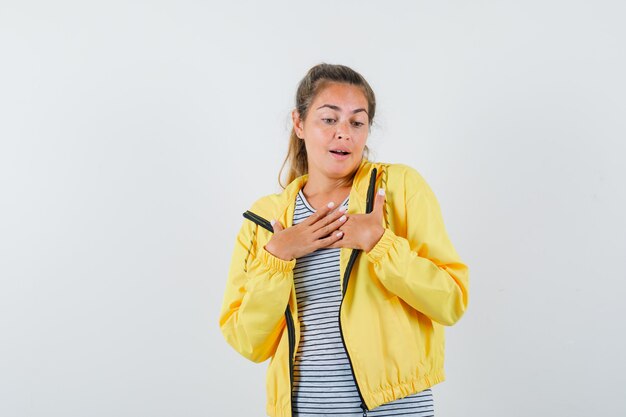 Mujer joven en camiseta, chaqueta cogidos de la mano en el pecho y mirando elegante, vista frontal.