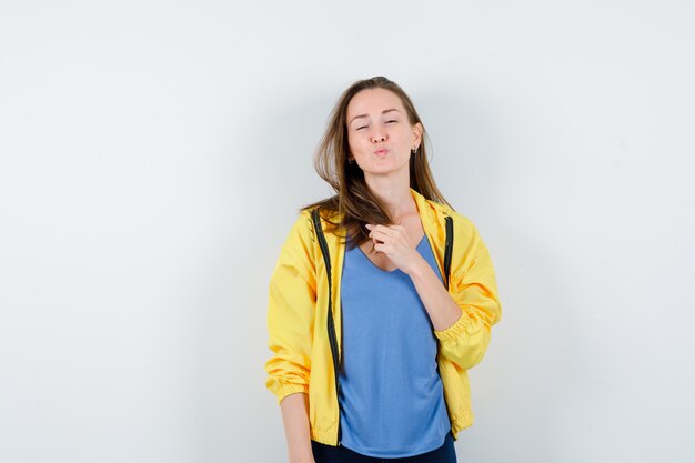 Mujer joven en camiseta, chaqueta haciendo pucheros, sosteniendo su mechón y luciendo delicada, vista frontal.