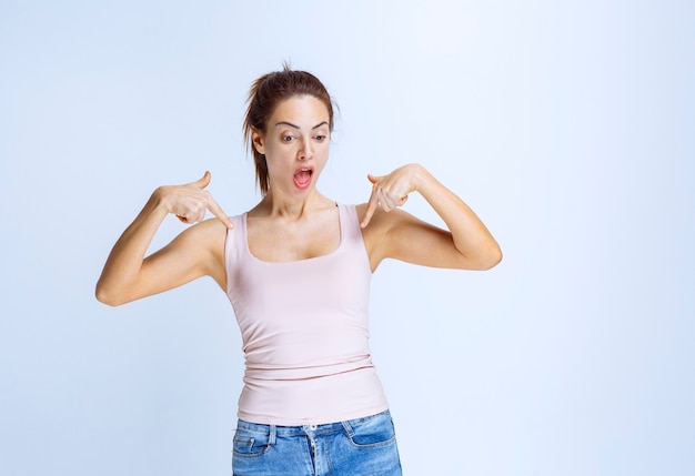 Mujer joven en camiseta deportiva apuntando a sí misma