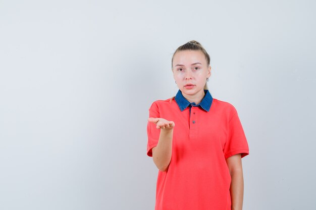 Mujer joven en camiseta estirando la mano en gesto de desconcierto