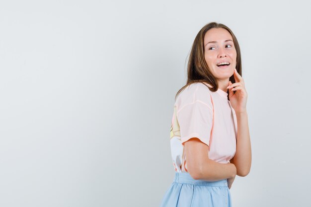 Mujer joven en camiseta, falda mirando hacia atrás y mirando curiosa, vista frontal.