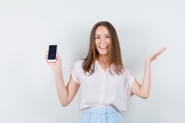 Mujer joven en camiseta, falda sosteniendo teléfono móvil y mirando contento.