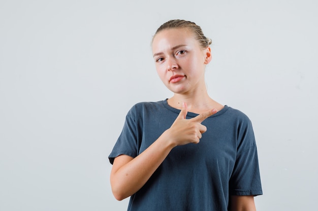 Mujer joven en camiseta gris apuntando hacia un lado y mirando con cuidado