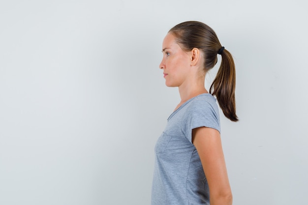 Foto gratuita mujer joven en camiseta gris cogidos de la mano en la espalda y mirando enfocado.