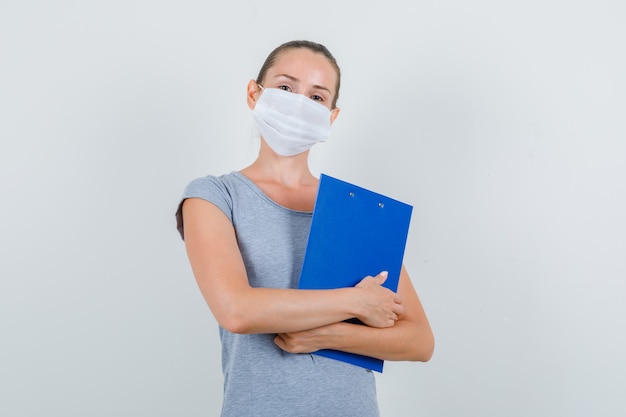 Mujer joven en camiseta gris, máscara con portapapeles, vista frontal.