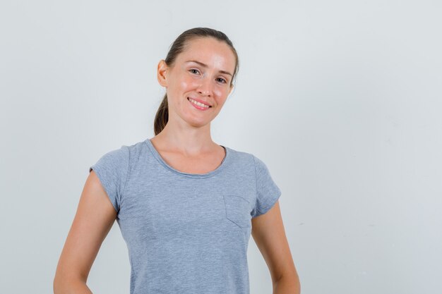 Mujer joven en camiseta gris mirando alegre, vista frontal.