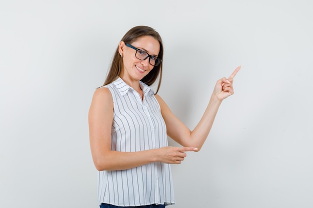 Foto gratuita mujer joven en camiseta, jeans apuntando hacia un lado y hacia arriba y mirando alegre, vista frontal.