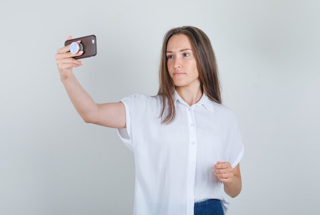 Mujer joven en camiseta, jeans tomando selfie en teléfono