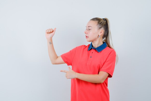 Mujer joven en camiseta levantando el brazo, apuntando hacia el lado y mirando enfocado